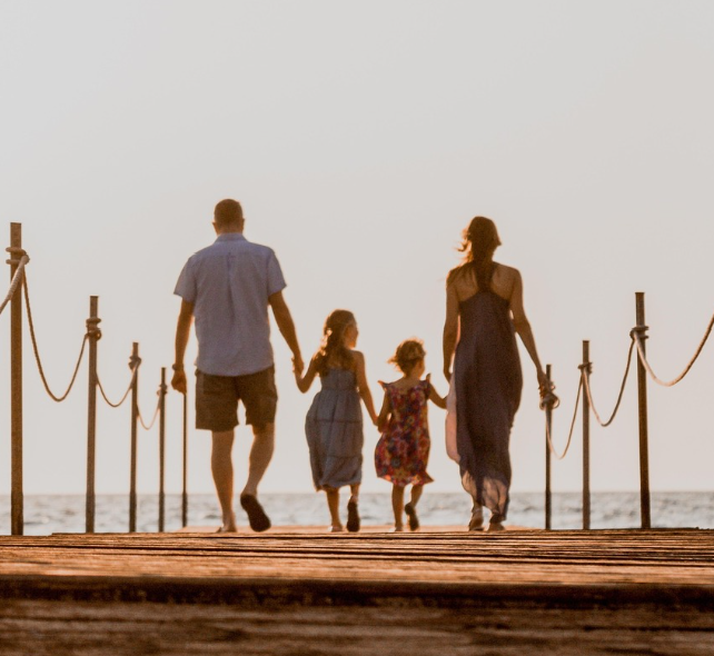 바닷가 산책길을 함께 걷는 부모와 두 아이의 가족 모습