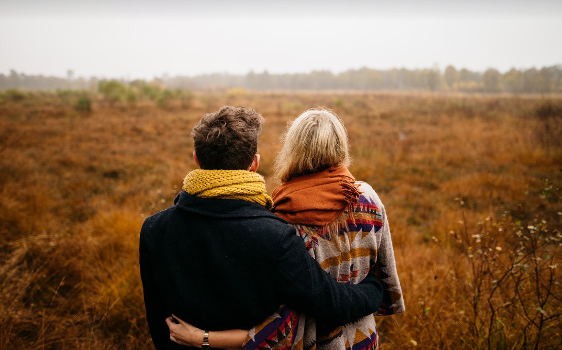 목도리를 한 연인이 서로의 허리를 감싸고 공원을 바라보고 있는 사진