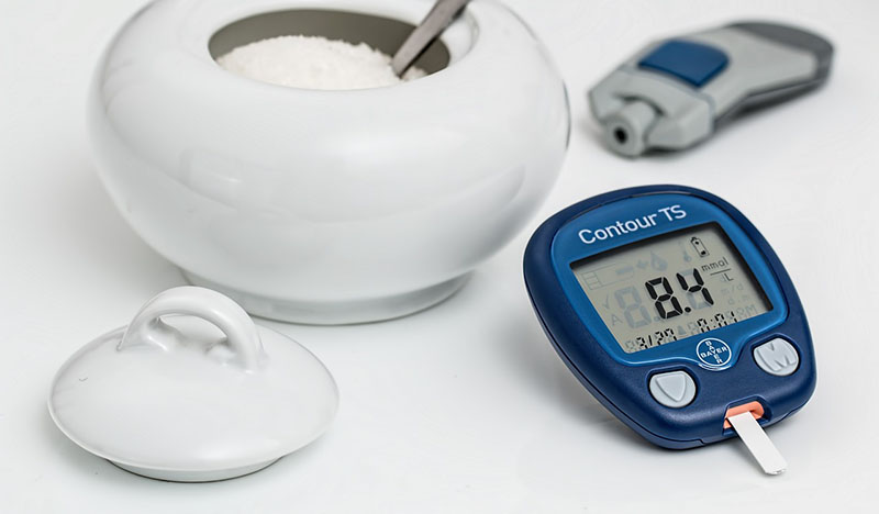 하얀 용기에 담긴 설탕과 옆에 있는 혈당 측정기