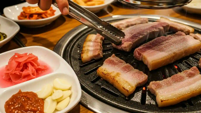 삼겹살을 불판에 굽고 있는 모습. 테이블 위 접시에 생강초절임이 있음