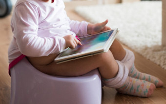 어린아이가 작은 유아용 변기에 앉아 태블릿을 사용하는 모습.