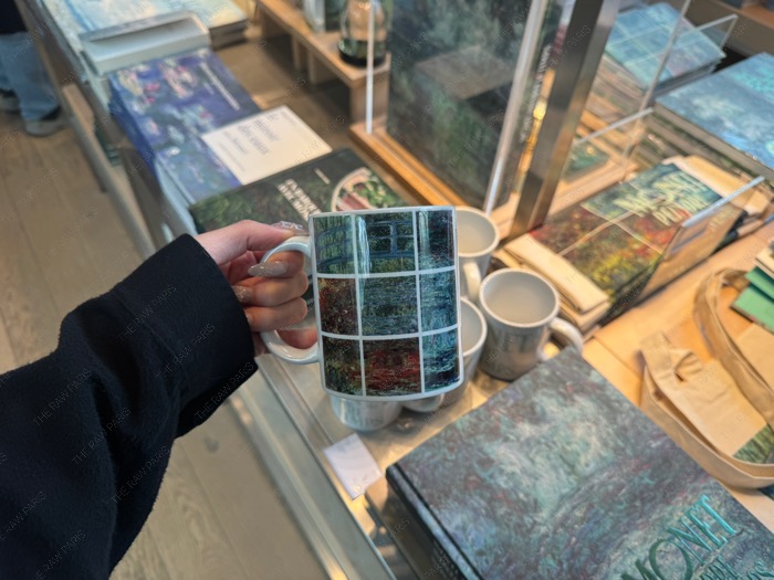 Hand holding a ceramic mug with 9-grid Monet Water Lilies graphics at Musée de l'Orangerie art shop.