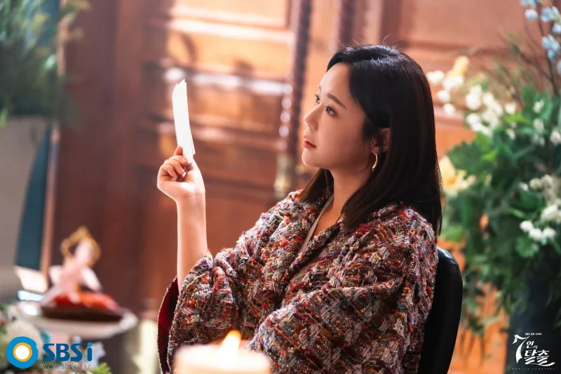 화분과 고급스런 어느 실내에 검은 긴 머리와 화려한 의상을 입고 앉아 있는 드라마 7인의 탈출의 금라희 캐릭터