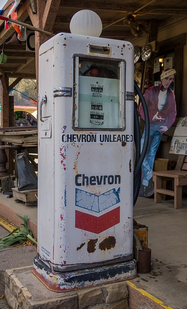 An old&#44; rusty chevron gas dispenser stands in front of a store.