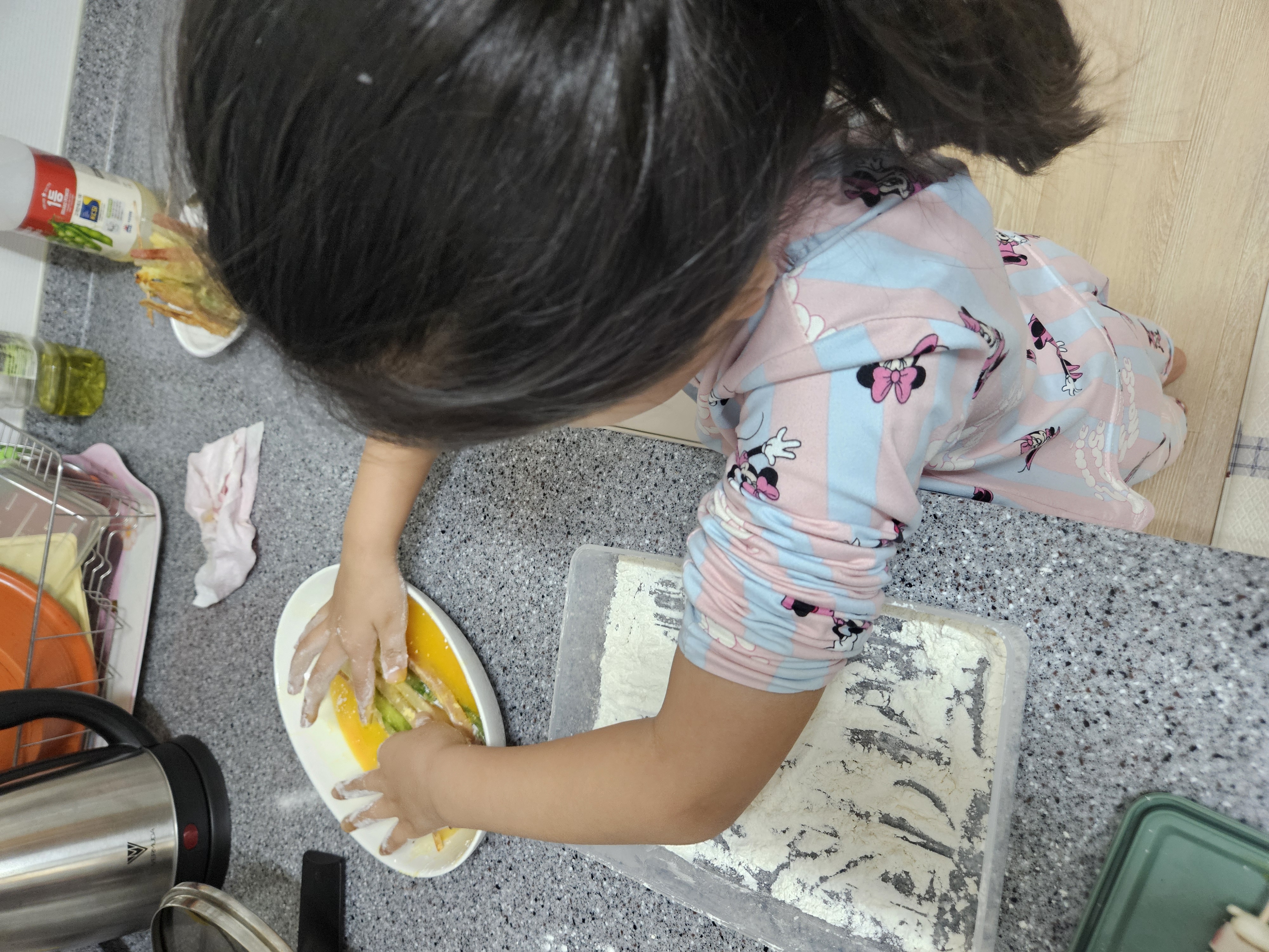 주방 조리대 앞에서 내복을 입은 아이가 집중해서 산적 재료에 밀가루와 달걀물을 묻히고 있는 뒷모습