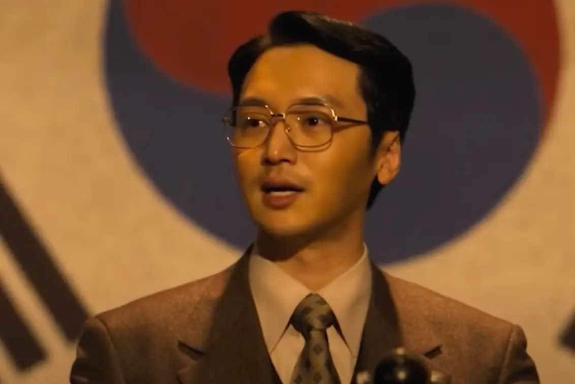 태극기 배경 갈색 양복을 입은 변요한이 연설하는 모습