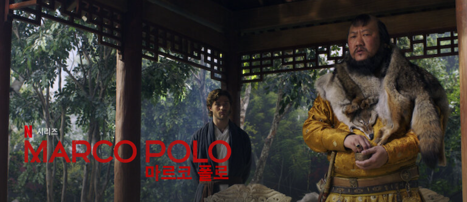 이 사진은 넷플릭스 드라마 마르코 폴로의 한 장먼으로 왼쪽에는 쿠빌라이 칸이 무언가 잡고 있고 그 뒤에는 마르코 폴로가 서있습니다. 배경은 숲이며 그 안에 있는 정좌같은 곳에 두명이 서 있습니다.