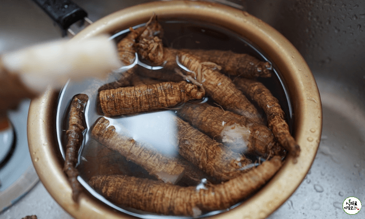 양은냄비-안에-물과-껍질을-까지않은-더덕들이-있고-그위로-껍질을-반만-깐-더덕을-손에-쥐고있다