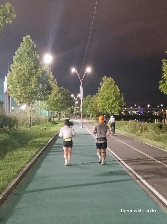 조명이 켜진 강변 트랙에서 올바른 슬로우 조깅 방법으로 대화 가능한 속도로 달리는 사람들