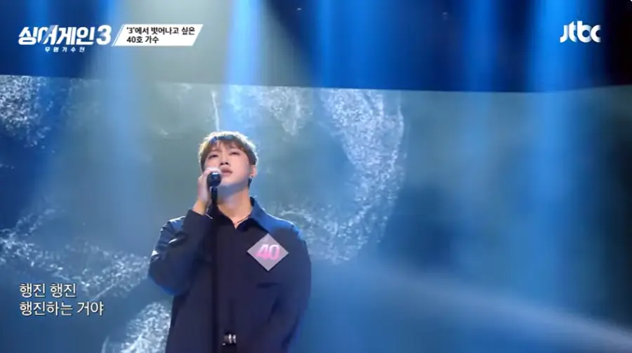 싱어게인3-
파란배경의 무대 검은 셔츠 왼쪽가슴에 숫자 30이 적힌 뺏지에 검은색 스탠딩 마이크를 오른손으로 잡고 정면을 바라보는 40호