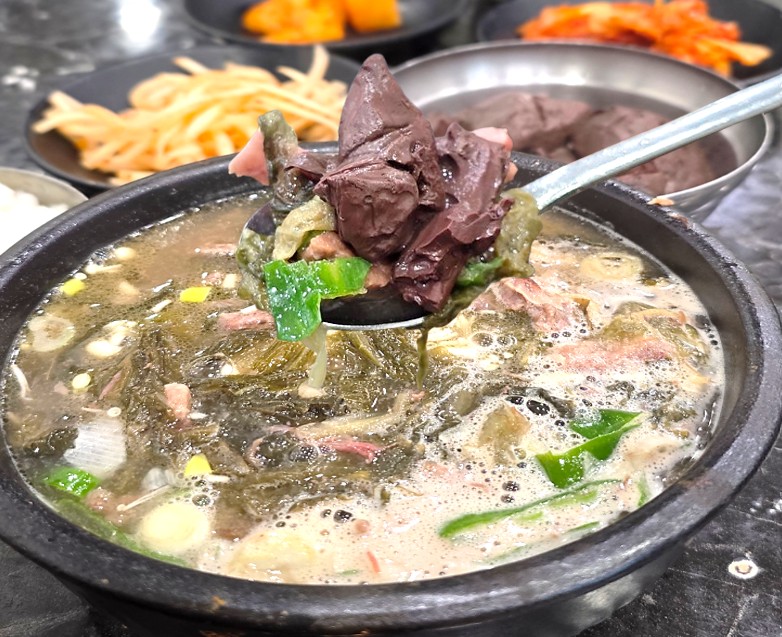뚝배기에 건더기와 국물이 가득 담겨져 있는 수원 해장국집 유치회관의 선지해장국을 한 숟가락 크게 뜬 모습