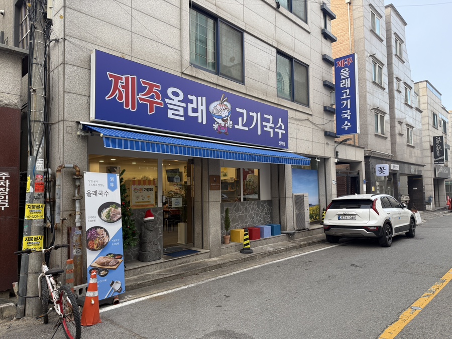 천안에 위치한 제주올래고기국수집의 외부 전경으로, 깔끔한 간판과 식당 입구가 보이는 사진. 제주 분위기가 느껴지는 간판 디자인이 특징이다.