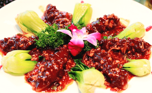 하얀 접시 위에 6마리 해삼이 갈색 소스를 듬뿍 묻힌 채 놓여있다. 해삼 사이마다 잘 익은 청경채가 있고 중앙에는 파슬리와 분홍색 꽃장식이 있다.