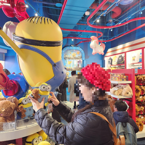 미니언즈 굿즈를 구경하는 사람들. 한 사람이 인형을 들어 올리고 있다.