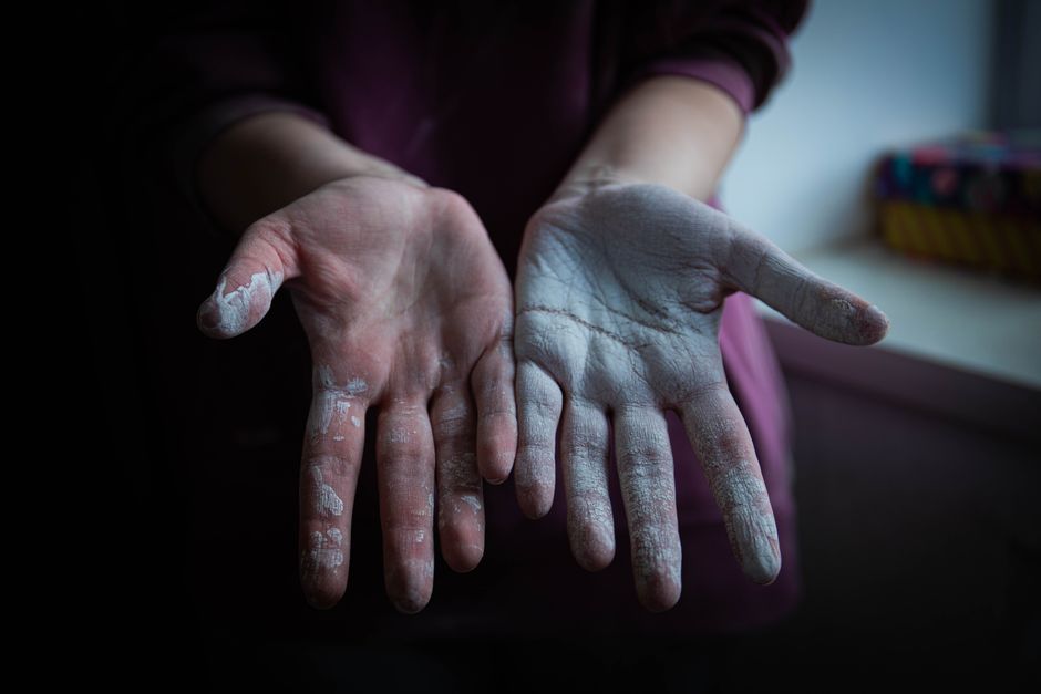 Close-up of chalk-covered hands extended in a dimly lit room, emphasizing texture.