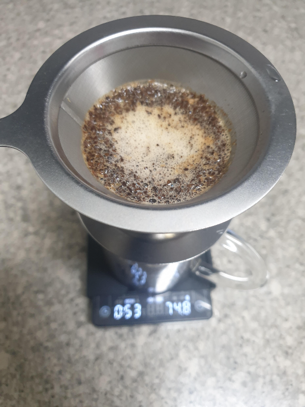 저울 위 금속 드리퍼, 금속 드리퍼 안에 물이 부어져 있는 커피 가루