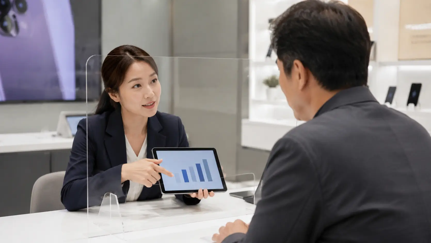 한국의 휴대폰 공식 대리점 창구에서 정장을 입은 여직원이 40대 남성에게 태블릿으로 합법적인 한도 전환 방법을 설명하는 모습