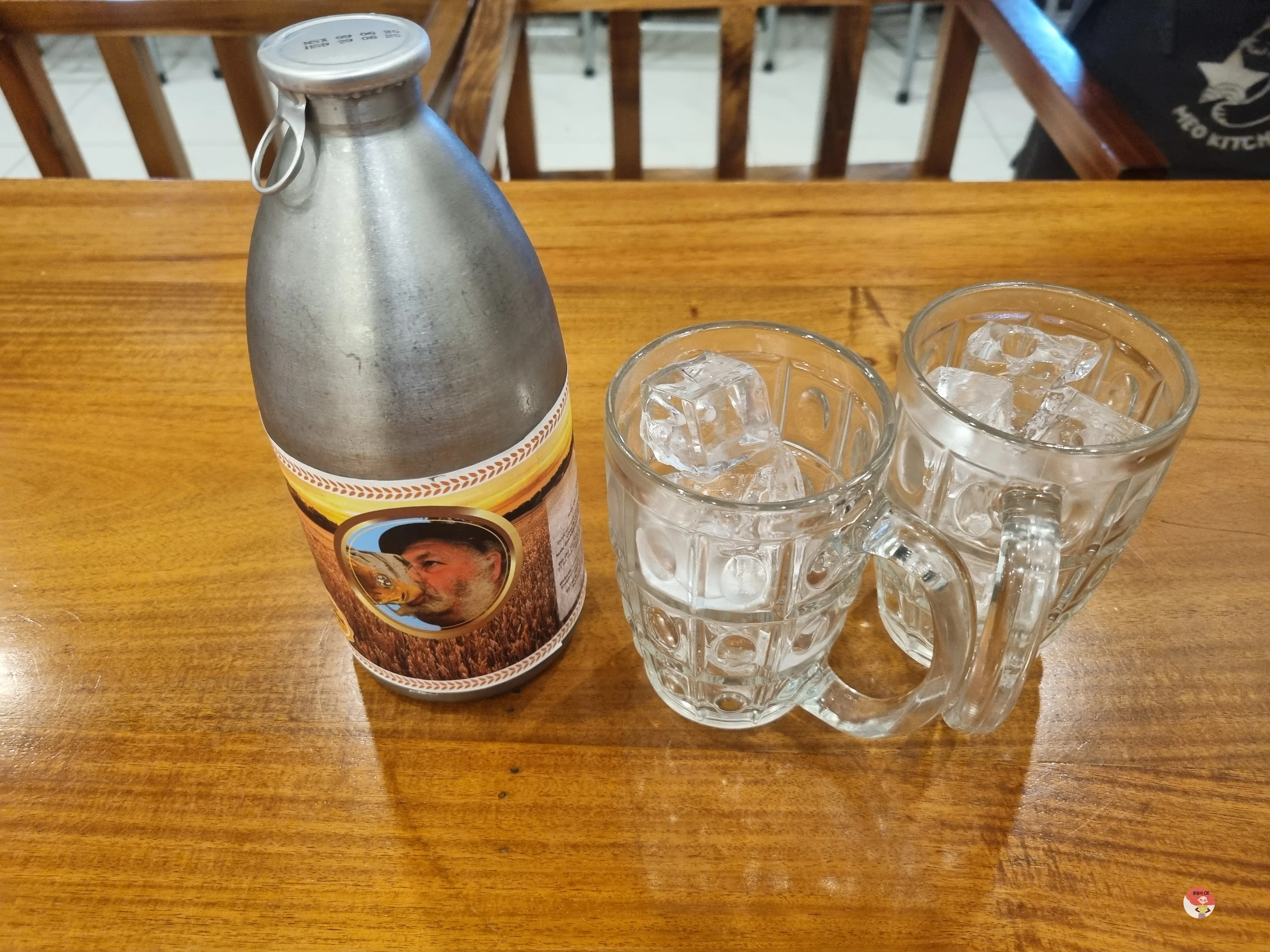 얼음이 담긴 유리잔 두 개와 사이공 맥주가 한 병 테이블 위에 놓여 있습니다. 병에는 맥주를 마시는 남성의 사진이 라벨로 붙어 있습니다.