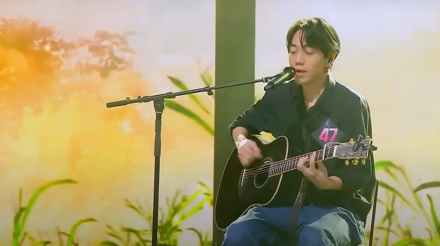 싱어게인3- 검은색 셔츠와 청바지에 가슴에 47번호표를 달고 검은색 기타를 치며 스탠딩마이크를 앞에 두고 앉아 노래하는 47호 옆모습