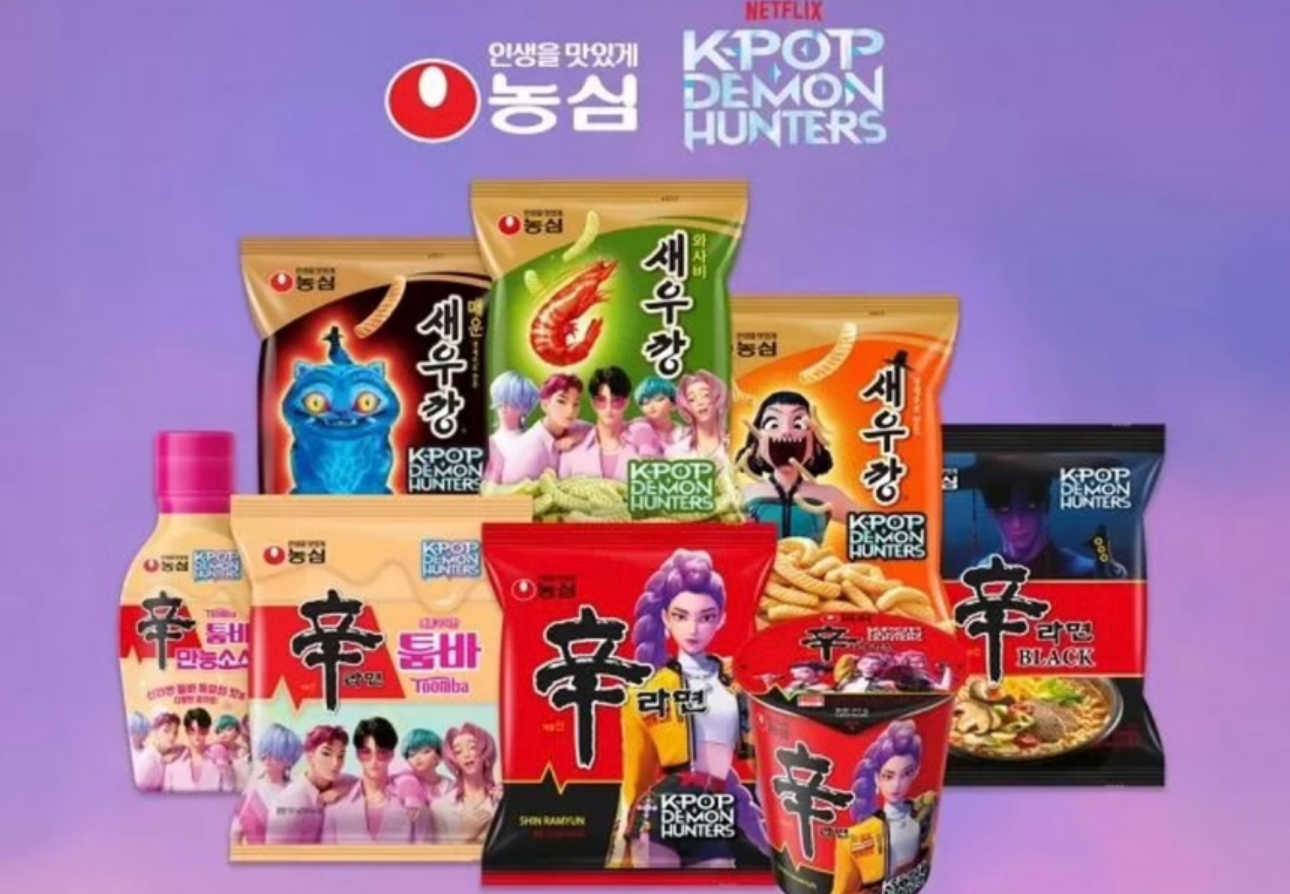 "농심 제품들이 진열된 광고 이미지. 새우깡, 신라면, 신라면 블랙, 신라면 컵라면, 신라면 소스, 신라면 퉁바 등 다양한 제품 포장이 보이며, 각 포장에는 넷플릭스 애니메이션 &lsquo;KPOP DEMON HUNTERS&rsquo;의 캐릭터들이 그려져 있다. 배경은 보라색 그라데이션."