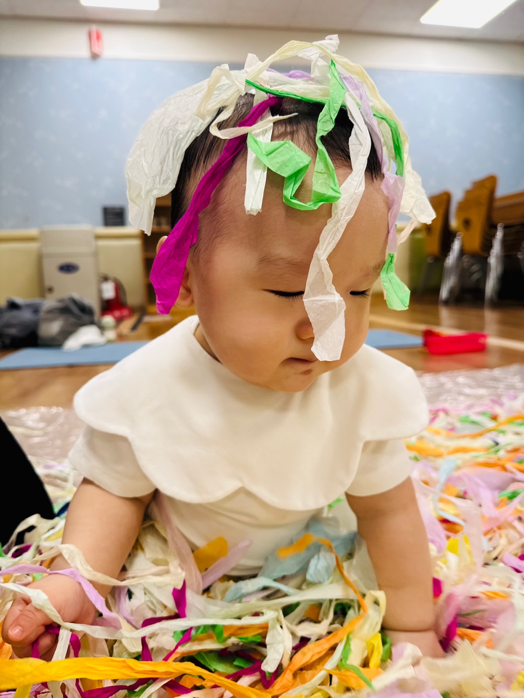 형형색색의 종이를 머리에 가득 뒤집어쓰고 장난스럽게 앉아있는 9개월 아기