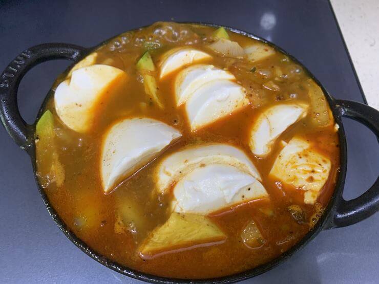 검은색 냄비 안에 빨간 국물과 순두부, 애호박, 양파가 함께 담겨져 있다.