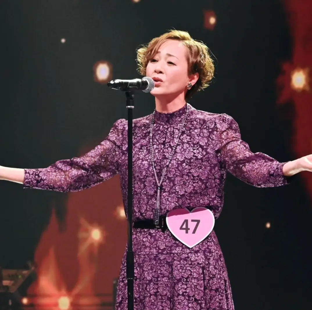 한일- 보라색 옷을 입고 무대 위에서 검은색 스탠딩 마이크를 앞에 두고 두팔벌려 노해하는 우타고코로 리에