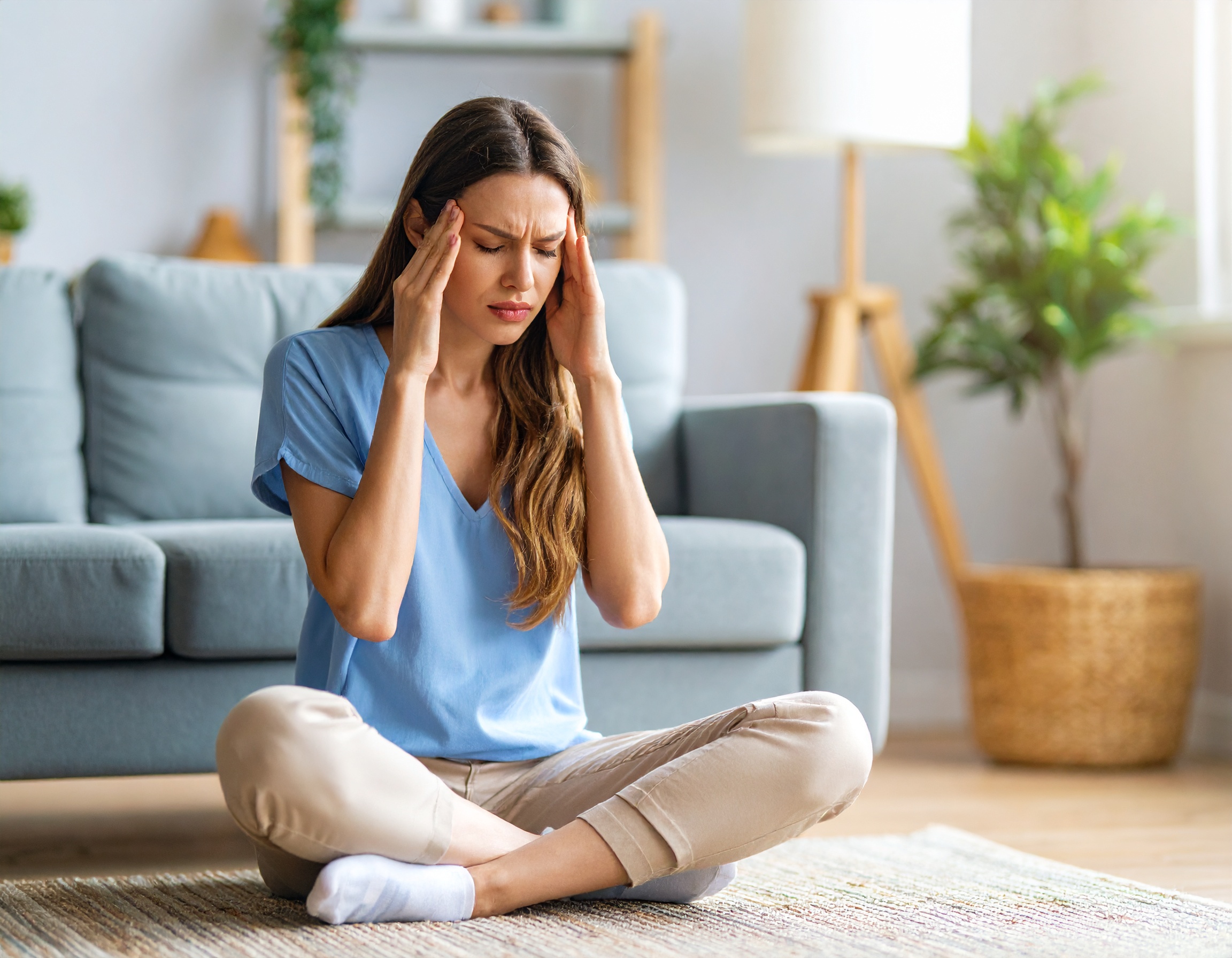실에서 양손으로 관자놀이를 누르며 두통을 호소하는 여성. 고혈압 초기증상 중 하나인 아침 두통의 예시