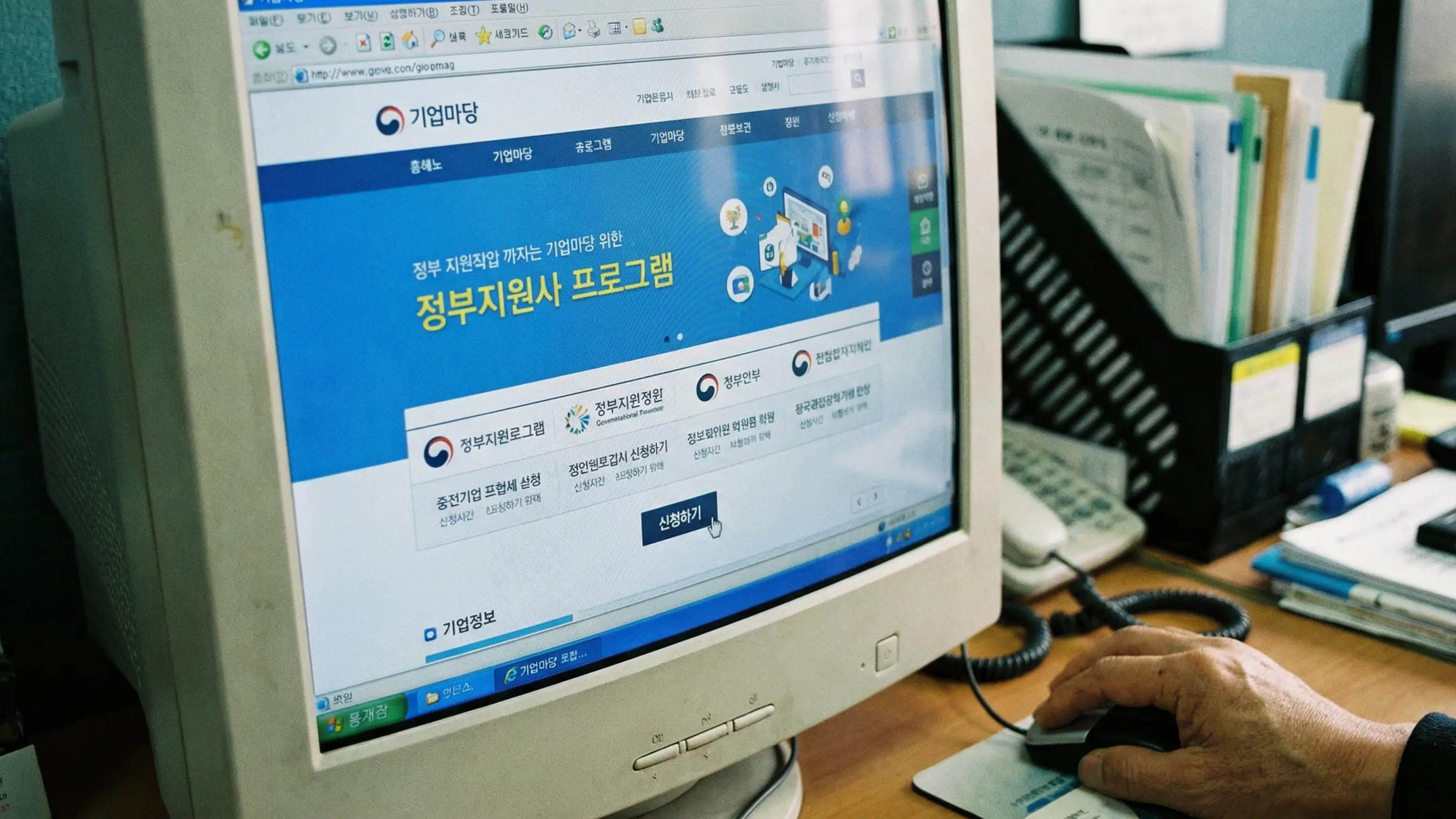 컴퓨터 화면에 띄워진 기업마당 홈페이지와 마우스로 신청 버튼을 클릭하는 손 클로즈업