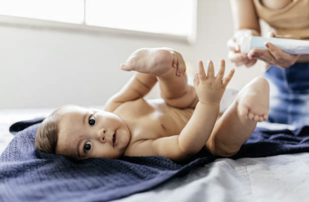 누워있는 아기의 엉덩이에 로션을 발라주는 모습