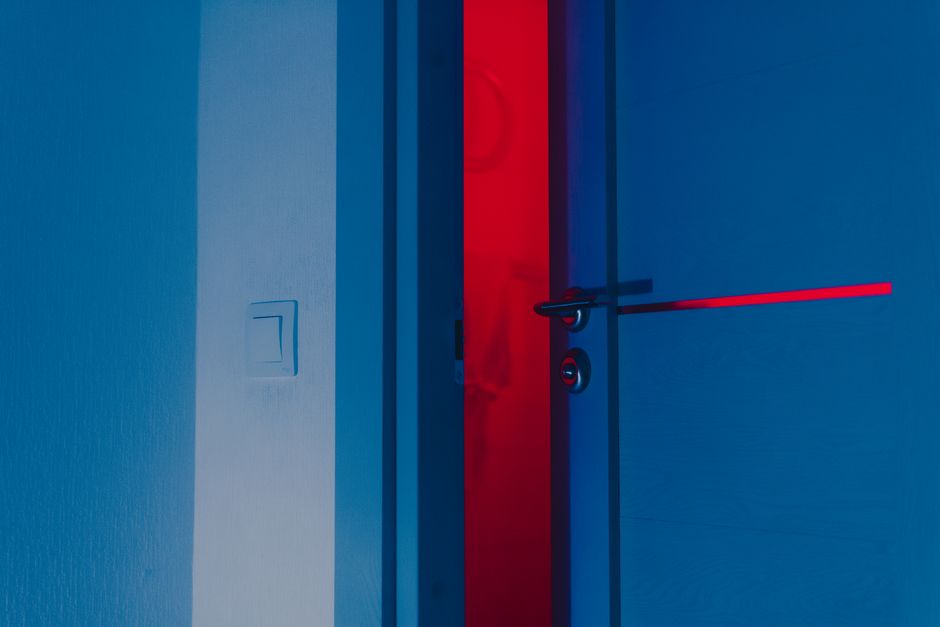 A half-open blue door illuminated by a dramatic red light reveals a unique interior atmosphere.