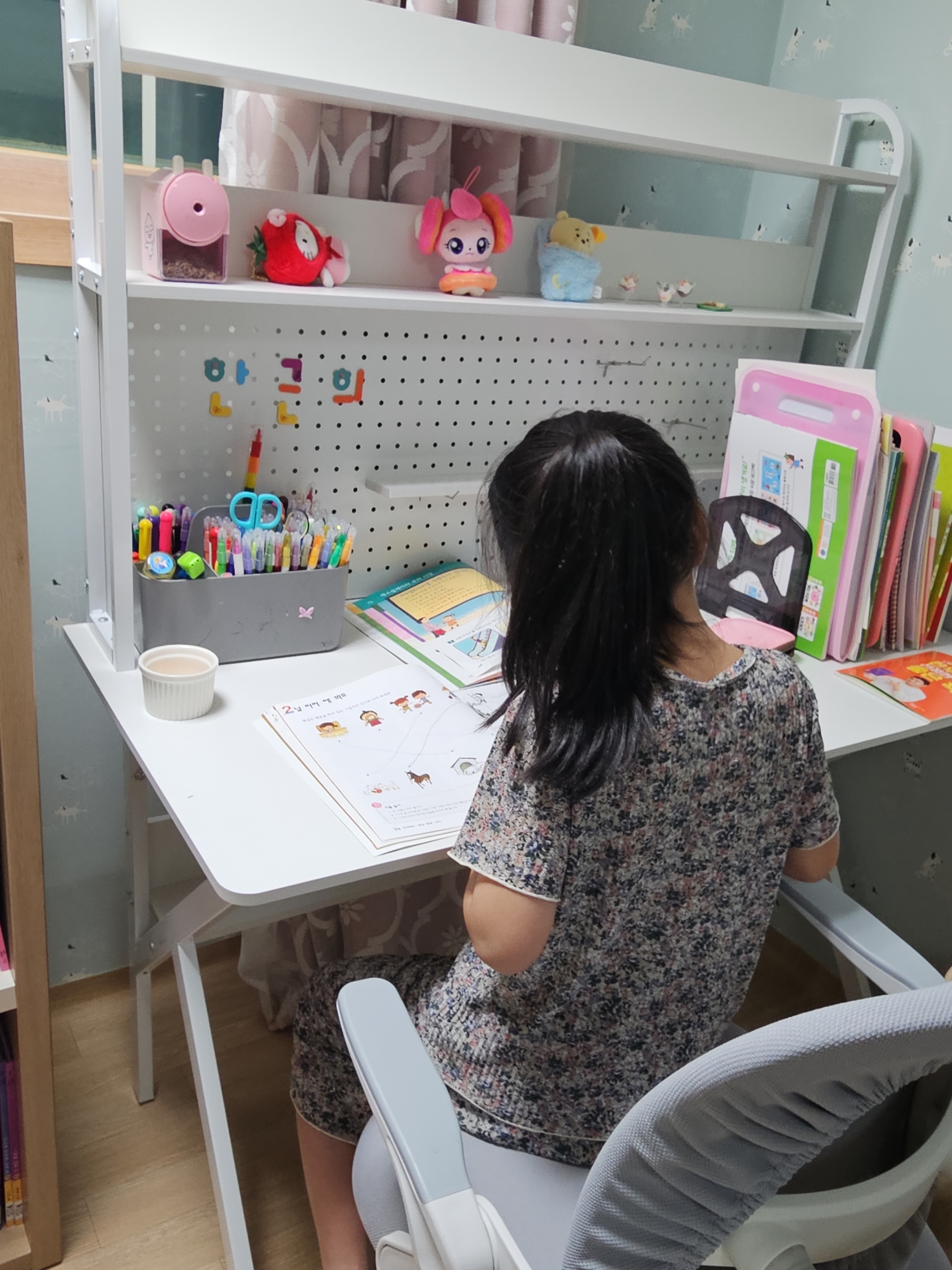 초등학생 아이가 책상에 앉아 불빛 아래에서 공부하는 뒷모습. 아이가 집중하면서 고개를 왼쪽으로 약간 기울이고 있는 모습이 보인다.