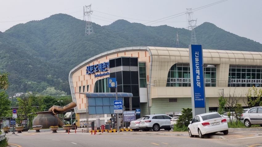 신둔도예촌역, 앞에는 주차차량들, 도자기 빚는 손, 항아리, 역 뒤로는 높은 산,