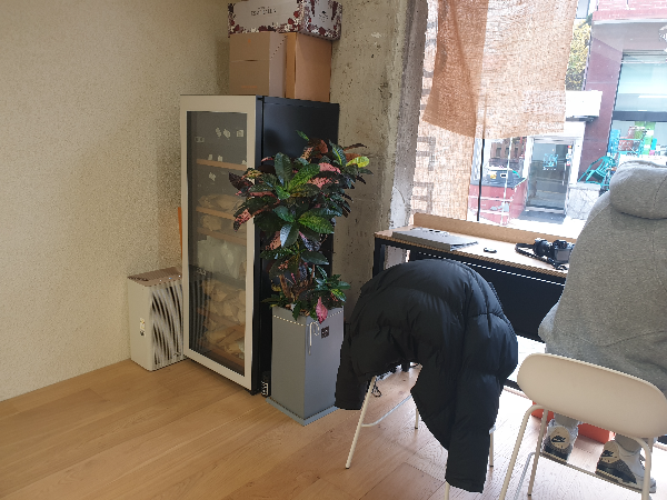 창을 바라보며 놓여있는 바형 테이블. 의자에 한 명의 고객이 앉아 있고 하나의 의자에는 패딩이 놓여있다.