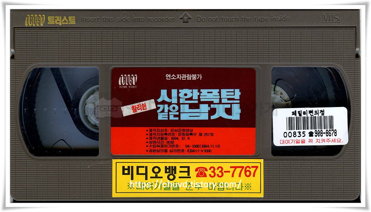 붉은 화염을 배경으로 결의에 찬 찰리 쉰의 얼굴과 크리스티 스완슨이 기대어 있는 1994년 작 '시한폭탄 같은 남자'의 낡은 대여점용 비디오테이프 이미지.