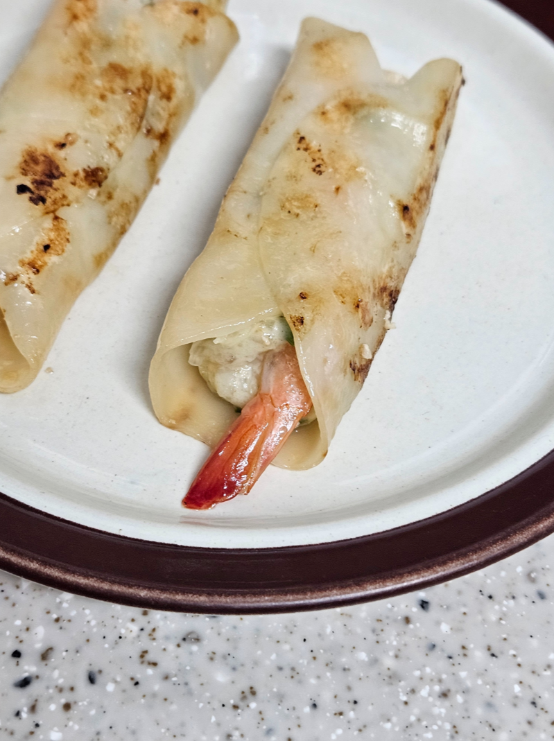 프라이팬에 조리한 비비고 통새우 만두를 접시에 담은 사진으로 새우 꼬리가 튀어 나와 있음
