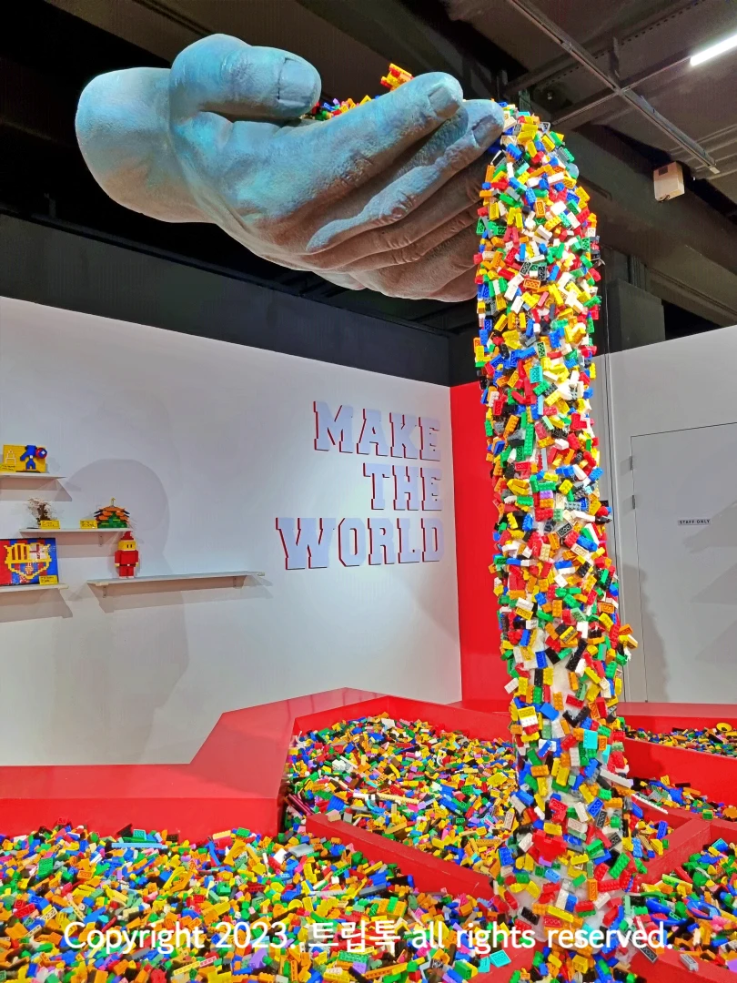 허공에 떠 있는 거대한 두손에서 수많은 알록달록한 브릭들이 떨어져 내리는 조형물