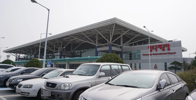 청주국제공항 건물이 뒤에 있고 앞에 차들이 주차되어 있다
