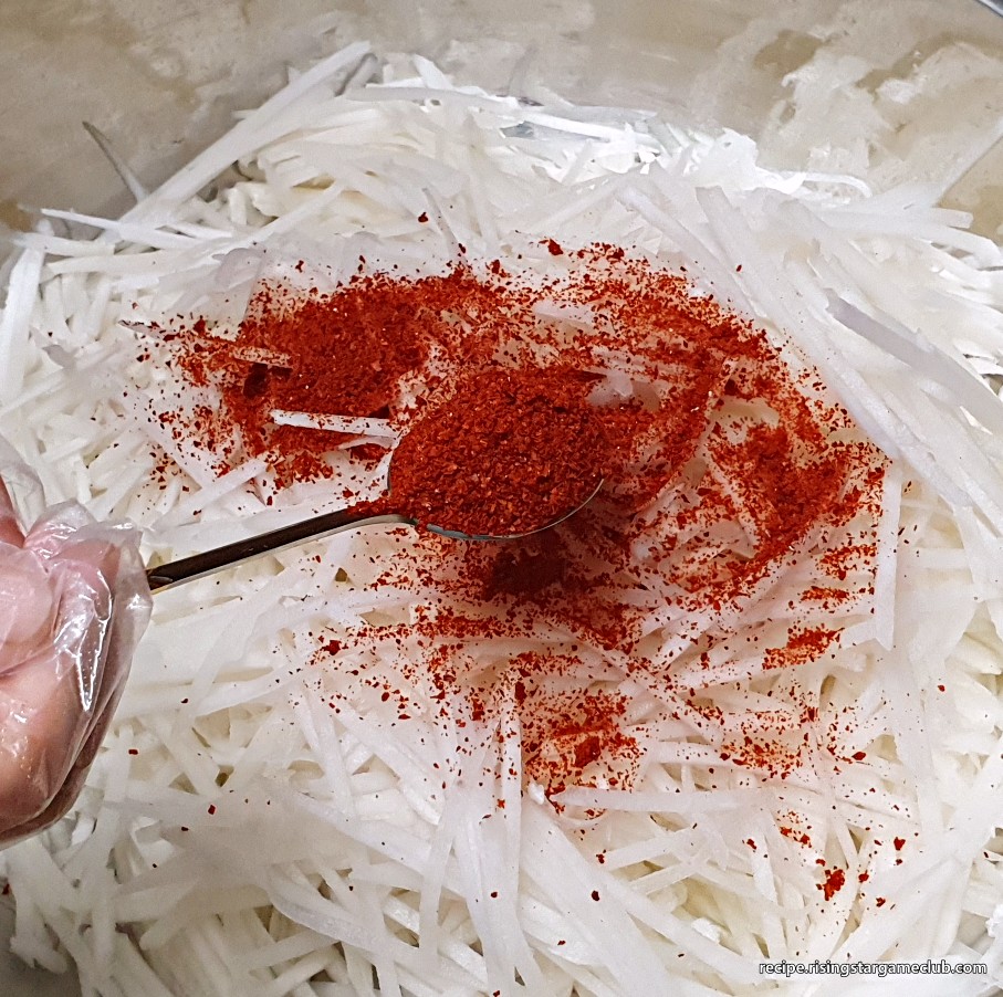 무생채 무침에 들어갈 무채를 양푼에 넣고 그 위에 고춧가루를 뿌리는 사진