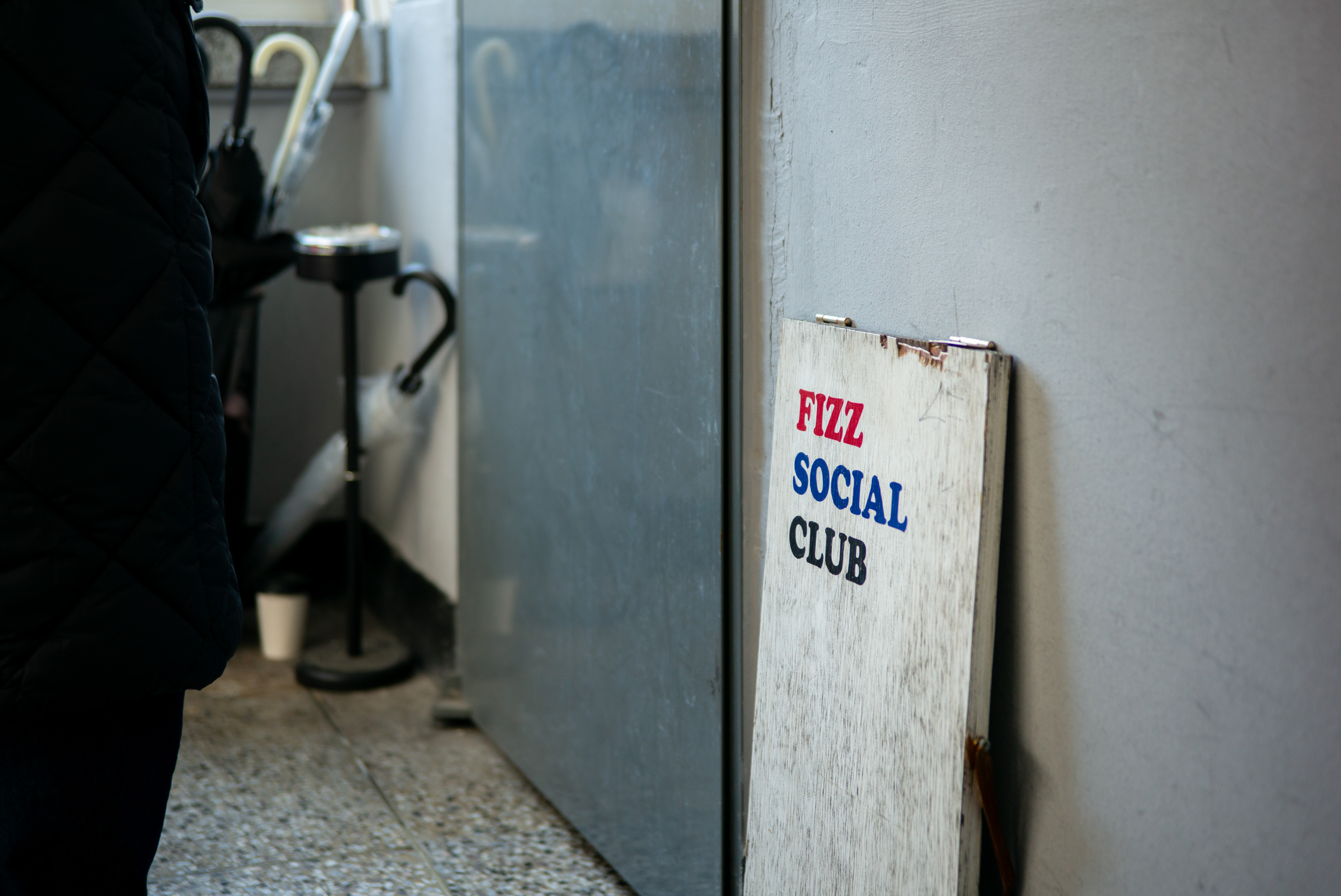 복도 구석에 놓인 'FIZZ SOCIAL CLUB' 표지판. 라이카 M-P 240의 차분한 그레이 톤과 질감 묘사.