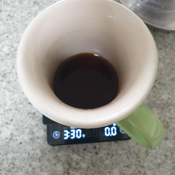 저울이 3분 30초를 가르키고 있다. 저울 위에는 커피가 조금 담긴 초록색 컵이 있다.