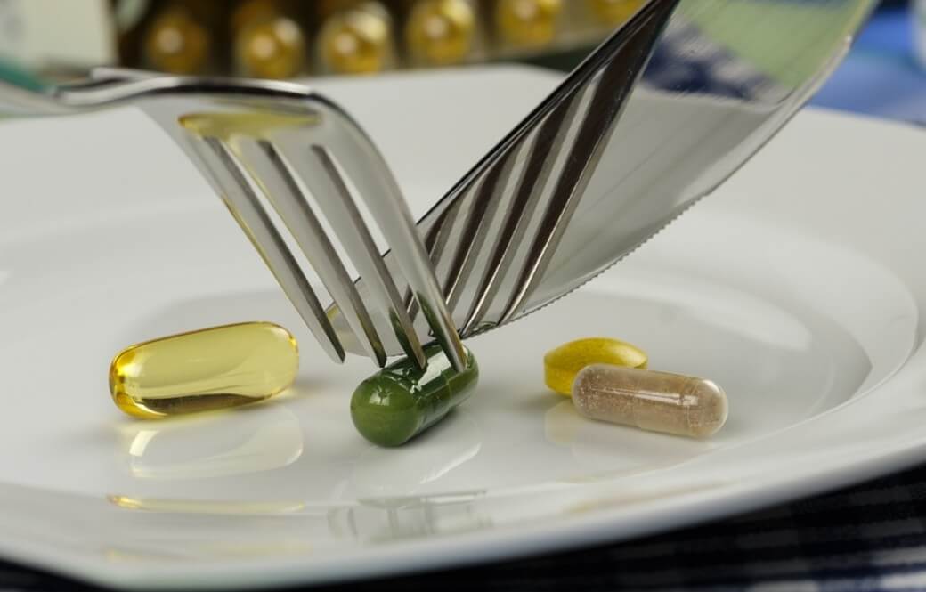 다이어트에 보조제 관한 것으로 접시에 여러개의 알약과 나이프와 포크로 알약을 자르는 사진입니다.