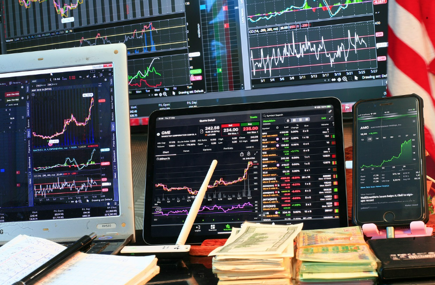 주식 차트가 띄워진 노트북, 핸드폰과 달러 다발