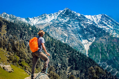 주황색 배낭을 매고 눈 덮힌 높는 산을 바라 보는 여행자 