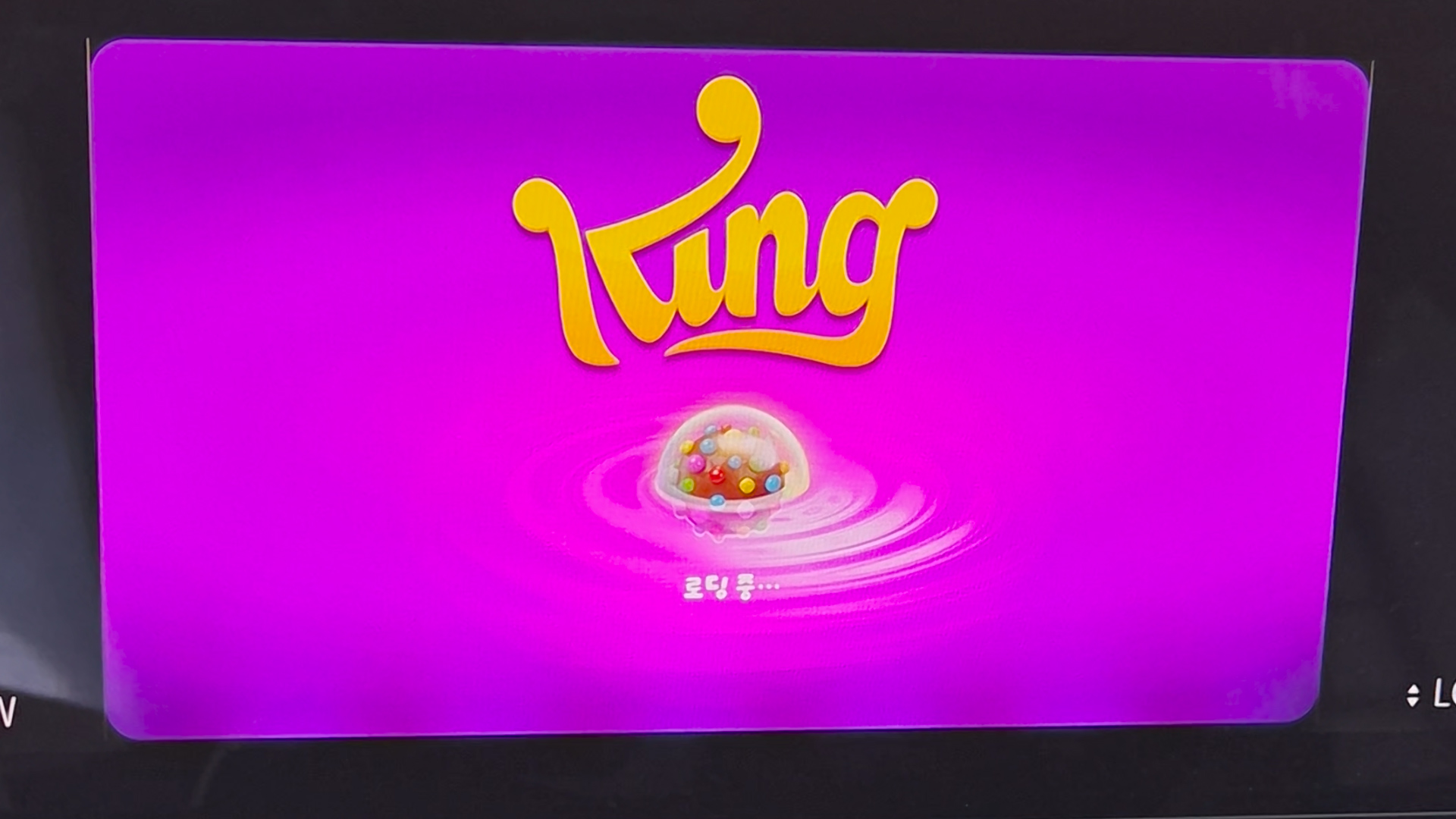 차량 디스플레이에 캔디크러쉬 소다 로딩 화면, King 로고와 컬러풀한 캔디볼이 보이는 장면