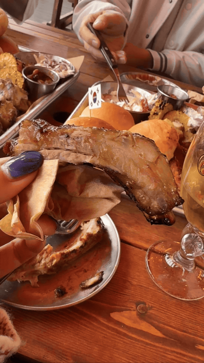 로코스바비큐 남양주점 3인 샘플러에서 나온 바베큐 한 손에 들고 흔들거리는 동영상 gif. 배경에서는 친구가 샐러드를 먹고 있다.