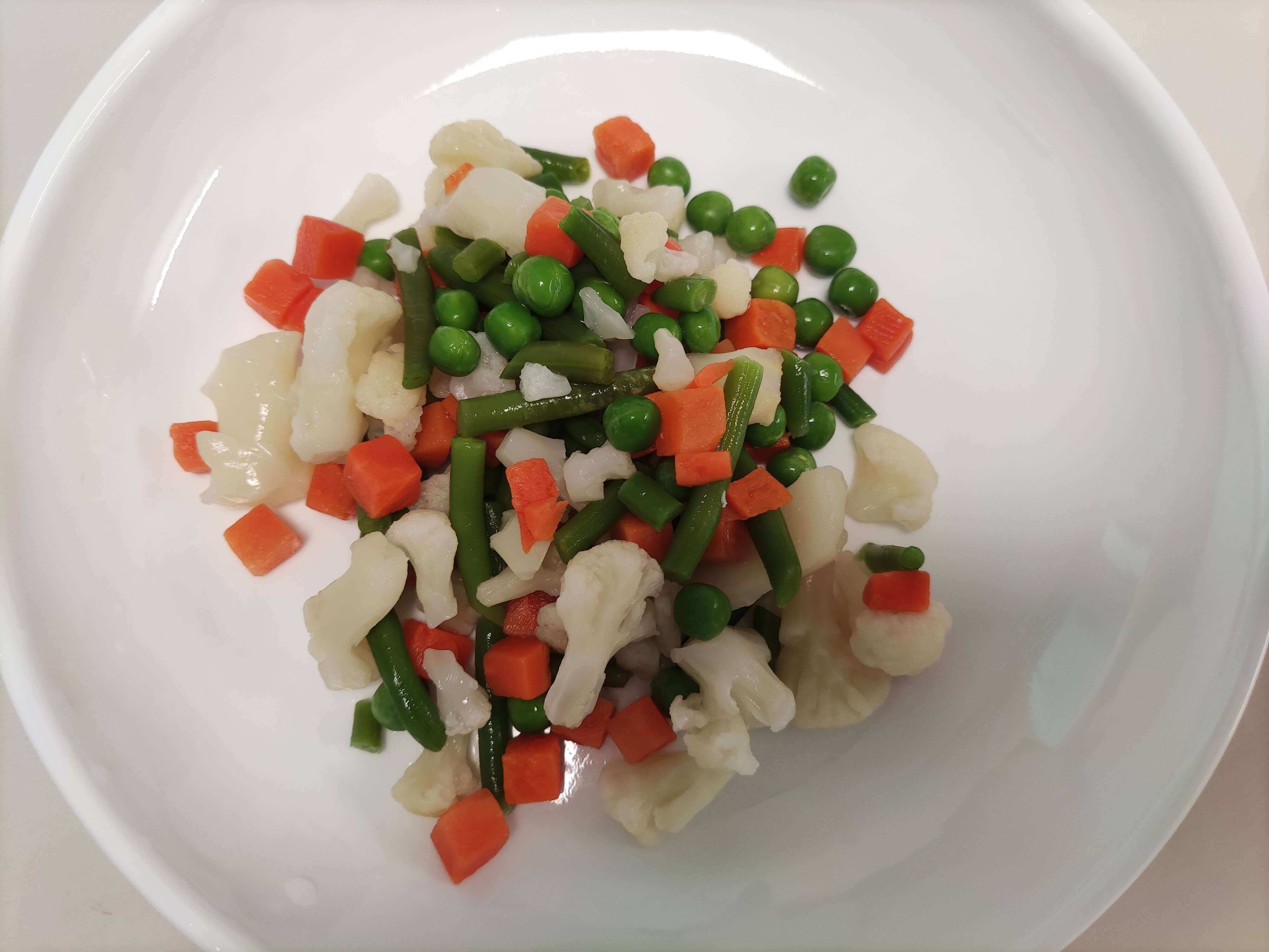 흰 접시에 담긴 냉동 채소 믹스 (콜리플라워, 그린빈, 당근, 완두콩)