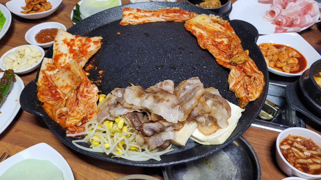 불판 위 삼겹살과 김치 콩나물 함께 굽는 모습