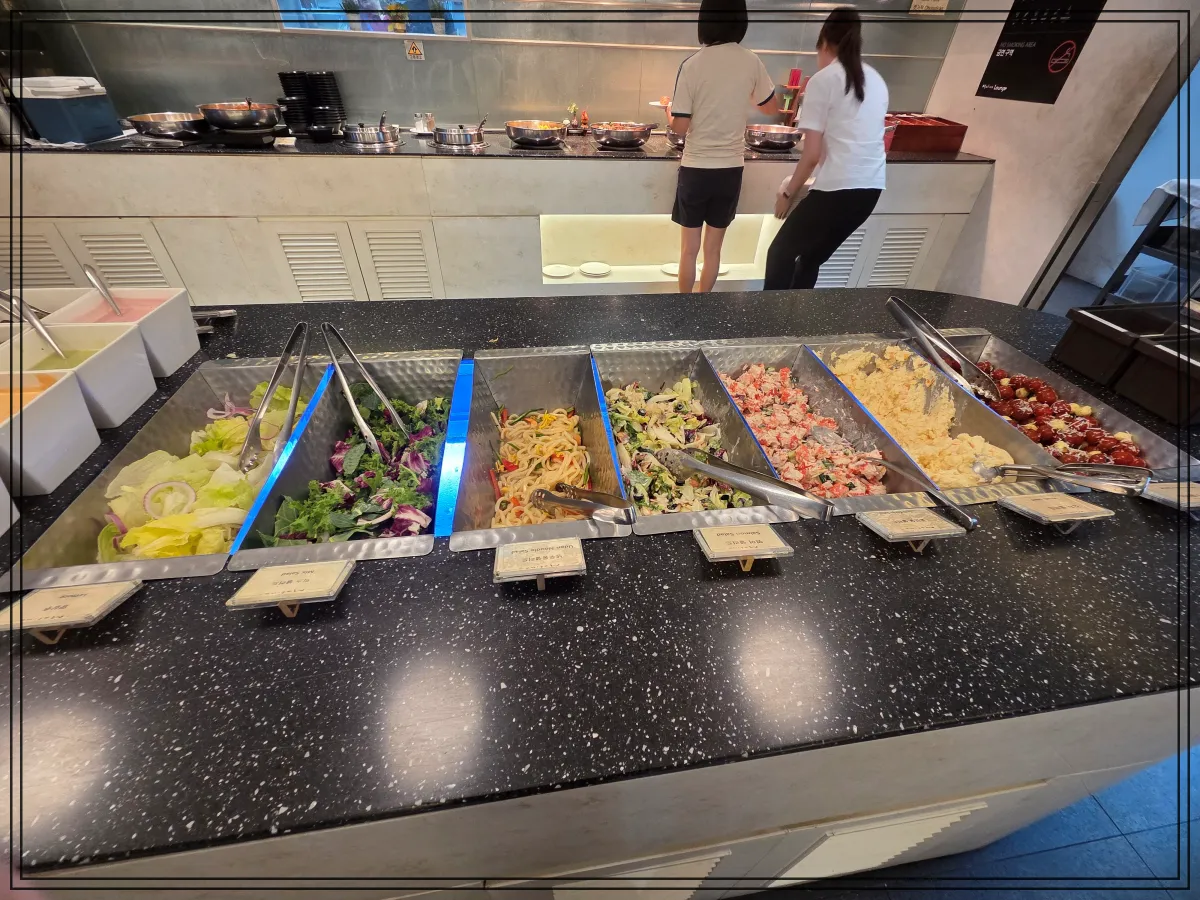 샐러드-바-중앙에-각종-샐러드와-파스타-계란-감자샐러드-방울토마토가-정돈되어-있고-뒤에-두-사람이-음식을-담고-있음