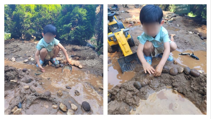 진흙탕에서 노란색 포크레인 중장비 장난감을 옆에 두고 돌과 흙으로 물길을 막으며 놀고 있는 아이